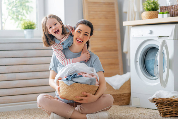 Beautiful young woman and child girl little helper are having fun and smiling while doing laundry at home. - Foto, Imagem
