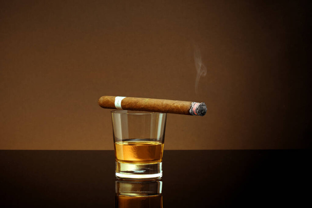 Vista cerrada del vaso de whisky con cigarro en la parte superior en la espalda de color - Foto, Imagen
