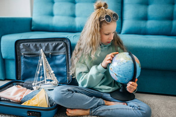 Onnellinen tyttö matkalaukku kotona. sininen laiva, meriloma, kartta ja maapallo. Matkustuskäsite. - Valokuva, kuva