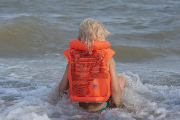 Gyerek ül egy narancssárga felfújható úszómellényben a tengerparton. Visszanézés. - Fotó, kép