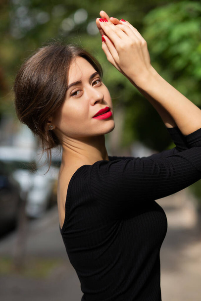 Чарівна елегантна брюнетка з червоними губами носить чорну сукню, позує на вулиці з сонячним світлом
 - Фото, зображення