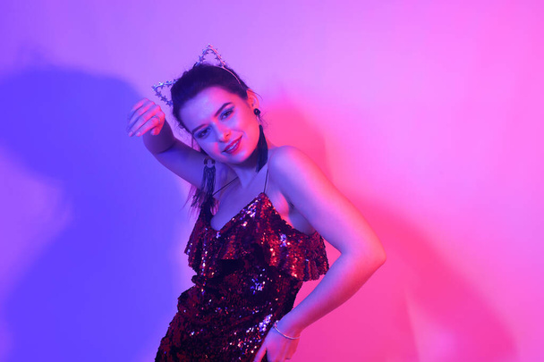 Gorgeous girl dancing in a neon light. A girl in a red shiny dress and with cat ears is dancing at a party. Smile dance in neon - Фото, зображення