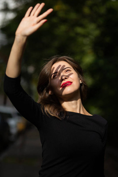 Stylish young woman with red lips covers her face from sun rays - Foto, afbeelding