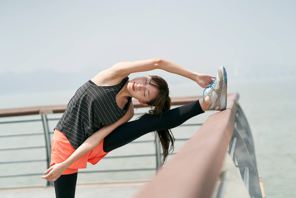 young asian woman in sportswear stretching body outdoors in seaside park - Photo, Image