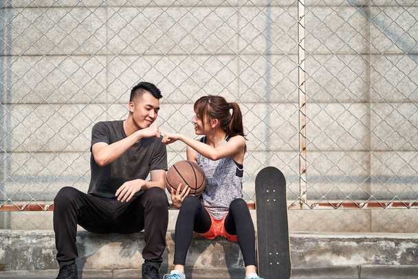 若いアジア系の成人男性と女性が野外バスケットボールコートで拳をぶつける - 写真・画像