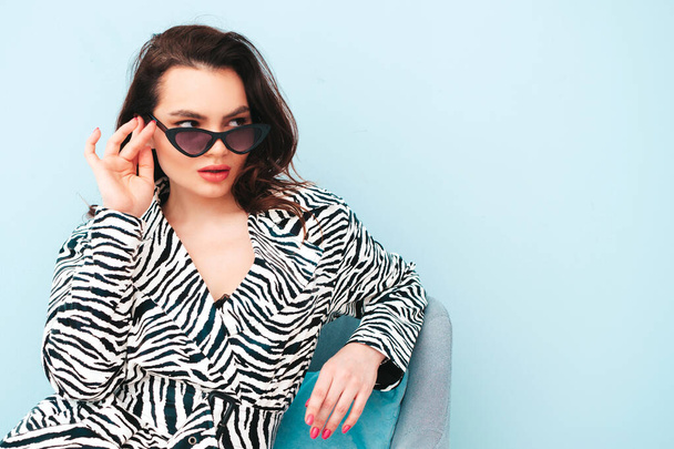 High fashion portrait of young beautiful brunette woman wearing nice trendy summer zebra coat.Sexy fashion model posing near light blue wall in studio.Fashionable female indoors in sunglasses - Photo, Image