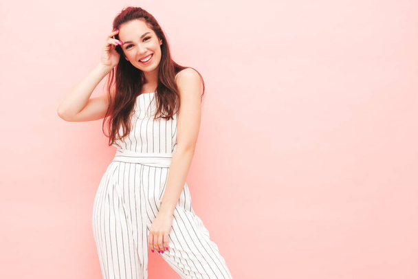 Portrait of young beautiful smiling female in trendy summer hipster overalls clothes. Sexy carefree woman posing near pink wall in studio. Positive model having fun indoors. Cheerful and happy - Photo, image