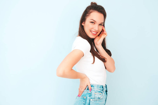 Young beautiful smiling female in trendy summer hipster clothes. Sexy carefree woman posing near light blue wall in studio. Positive model having fun indoors. Cheerful and happy  - Foto, imagen
