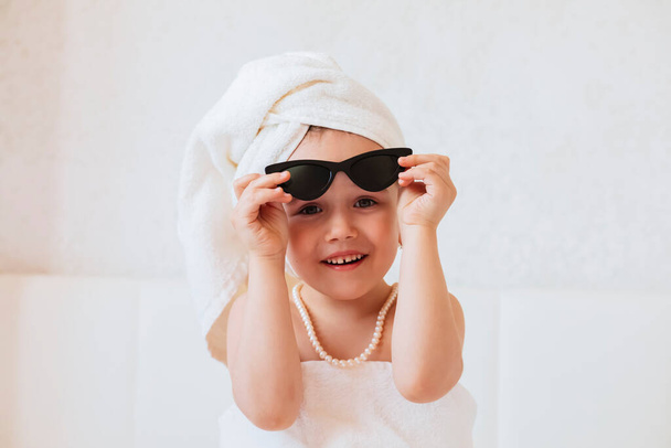 portrait of a cute little girl in a white bathrobe and a towel on a light background - Valokuva, kuva