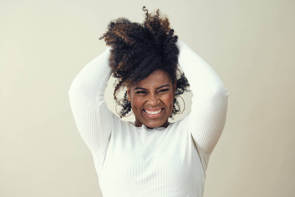 Cheerful Afro woman with hands in hair smiling against white background - Foto, Imagem