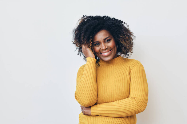 Πορτρέτο του χαμογελαστού όμορφη Afro γυναίκα στέκεται με τα χέρια σταυρωμένα, ένα χέρι στα μαλλιά - Φωτογραφία, εικόνα