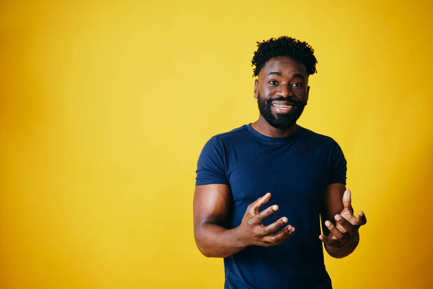 Portrait of playful Afro man smiling against yellow background - 写真・画像