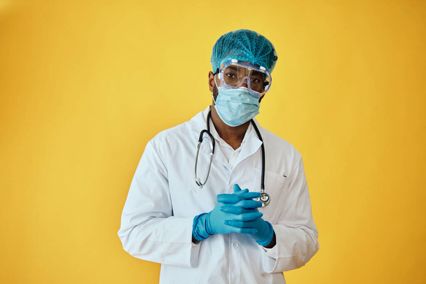 A COVID-19 elleni védelmet viselő férfi orvos portréja sárga háttér ellen - Fotó, kép