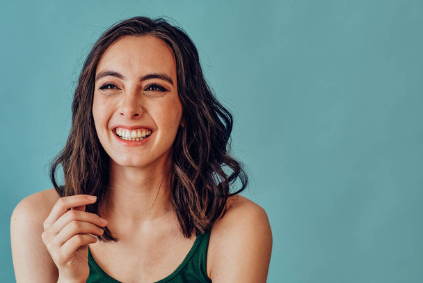 jonge vrouw glimlachen weg te kijken op blauwe achtergrond studio schot - Foto, afbeelding