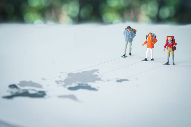 Miniaturní lidé batohem stojící na mapě světa s linií do cíle. Obrázek použití pro cestování na různých místech, cestovní koncept - Fotografie, Obrázek