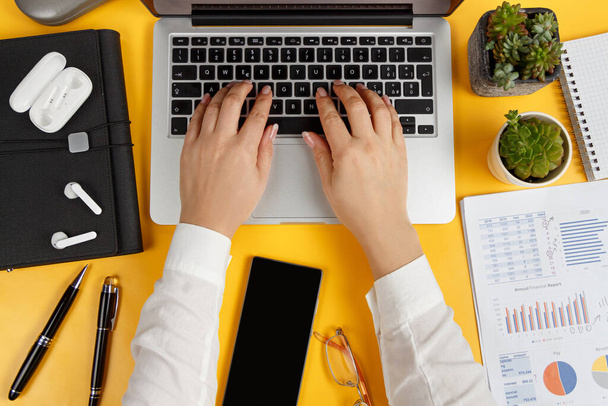 Modern ofis sarı masası ve iş kadını elleri dizüstü bilgisayarı görüyor. - Fotoğraf, Görsel