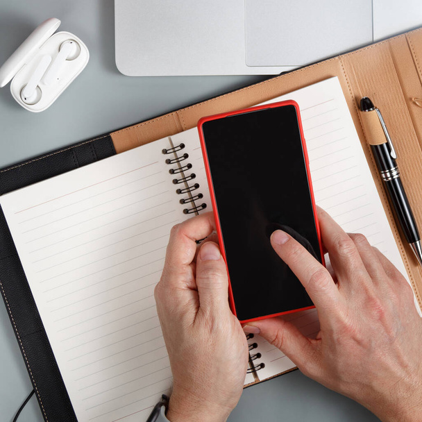 Homem escrevendo na agenda e usando telefone celular em uma mesa de escritório cinza vista superior. Conceito de negócio - Foto, Imagem