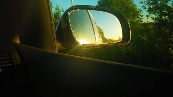 Θέα μέσα από τον πλευρικό καθρέφτη του αυτοκινήτου. Το ταμπλό. Το παρμπρίζ. Σύστημα πολυμέσων. Ο ήλιος. Η φύση. Πλευρικό παράθυρο. Πλευρικός καθρέφτης. - Φωτογραφία, εικόνα