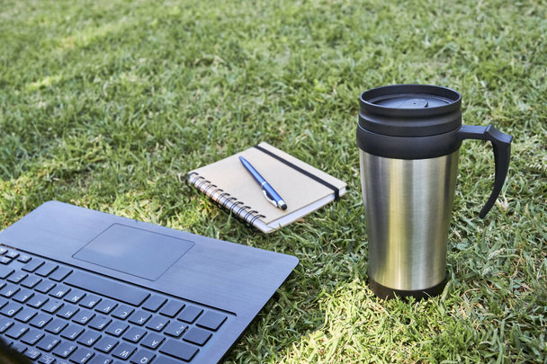 草の上での仕事や研究の要素,屋外:オープンラップトップ,ペンと生態学的に再利用可能なサーマルカップとノートブック.生態学と持続可能性の概念. - 写真・画像