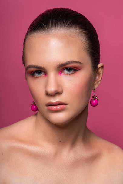 High beauty photo of a lovely young girl with wonderful professional makeup, round pink earrings, with long brown hair. Posing over rosy background. Close-up. Studio shot. Portrait - Φωτογραφία, εικόνα