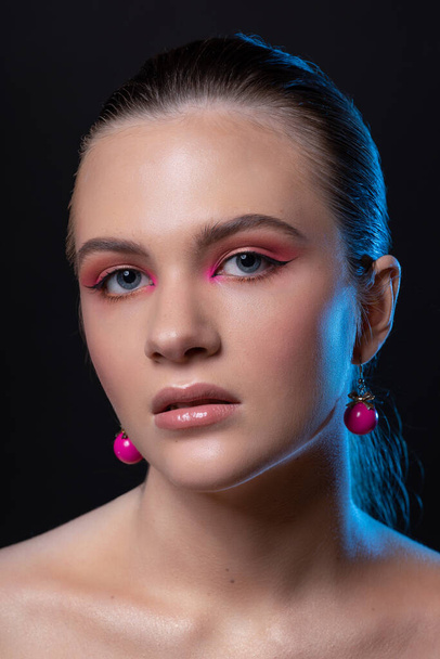 High beauty photo of a lovely young girl with wonderful professional makeup, round pink earrings, with long brown hair. Posing over black background. Close-up. Studio shot. Portrait - Fotó, kép