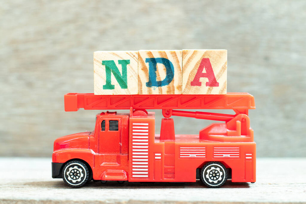 Feuerwehrleiterwagen halten Buchstabenblock in Wort NDA (Abkürzung für Geheimhaltungsvereinbarung) auf Holz-Hintergrund - Foto, Bild