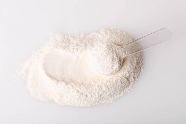 Montón de polvo de proteína blanca con cuchara dosificadora sobre fondo blanco. - Foto, Imagen