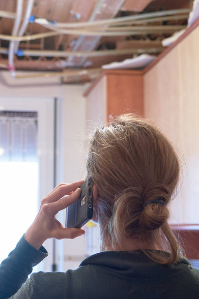 Zadní pohled na ustaranou ženu volající domů pojištění, protože se zhroutil strop kuchyně. Koncept domácí nehody - Fotografie, Obrázek