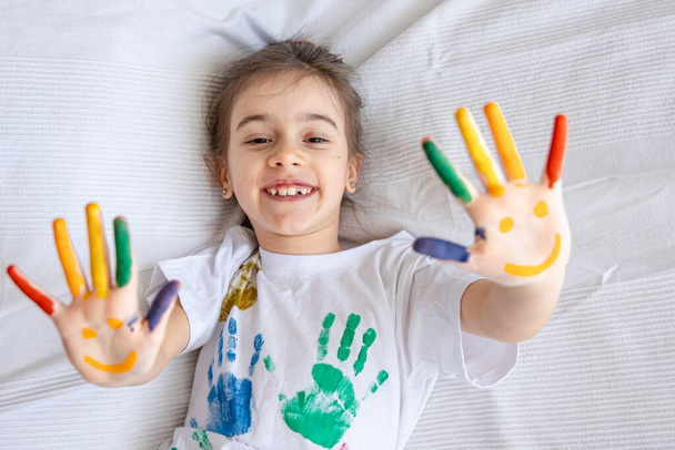 Gemaltes Lächeln auf den Handflächen eines kleinen Mädchens. Lustige bunte Zeichnungen auf Kinderhandflächen. - Foto, Bild