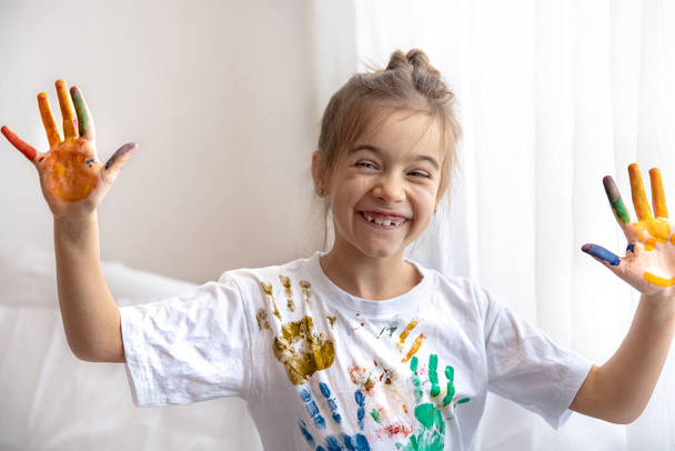 Pieni tyttö, jolla on kämmeniä maaleissa, suunnittelee T-paitaa, jossa on jälkiä kämmenistä. Lasten luovuus ja taide. - Valokuva, kuva