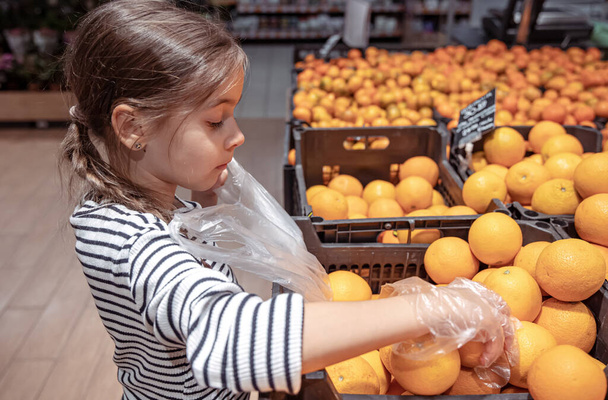 Una niña divertida en una tienda de comestibles elige naranjas para comprar. - Foto, Imagen