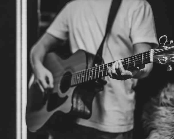 Un hombre toca una guitarra acústica en un cuarto oscuro. Actuación en vivo, concierto acústico, práctica. - Foto, imagen