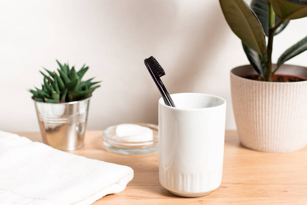 Cepillo de dientes negro en un vaso, toalla blanca, plantas caseras con espacio para copiar en un baño moderno y ligero. - Foto, Imagen