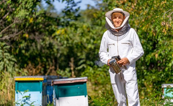 Man examining hives in summer. Agricultural beekeeper in protective cloth posing for camera. - Valokuva, kuva