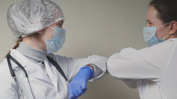Ärztinnen begrüßen sich mit den Ellbogen, der Arzt zieht blaue Schutzhandschuhe über die Hände, Schutz vor dem Virus bei der Verhinderung des Eindringens in die Atemwege der Lungen - Foto, Bild