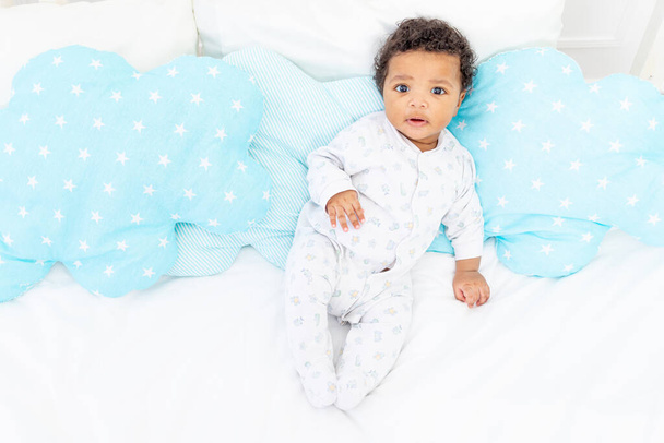 African-American little child on a white bed in the bedroom is lying in pajamas - Фото, зображення