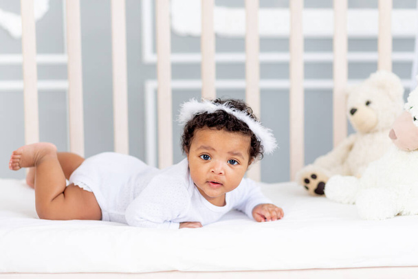 cute African-American little baby lying in bed for sleeping with angel headband - Foto, Imagem