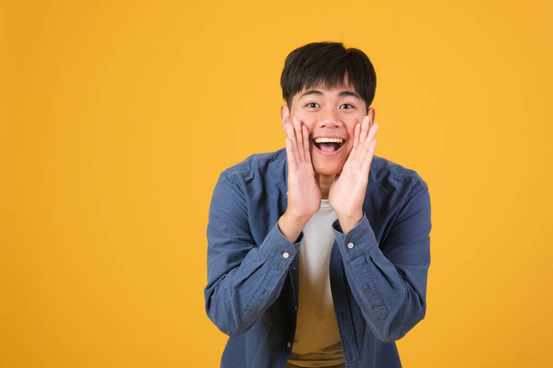 retrato de excitado asiático joven mantenga la mano boca grito grito aislado en amarillo naranja color fondo. - Foto, Imagen