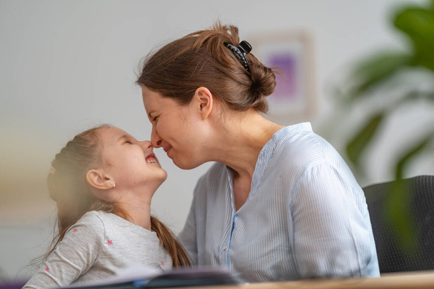 loving mother hugs and kisses her daughter. woman works from home office. woman and cute child are sitting at table. freelancer who uses laptop and Internet. concept of maternal love and care - Фото, зображення