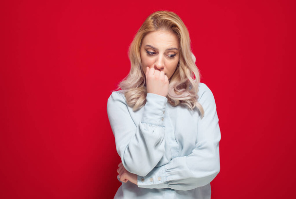 Worried young woman hold her hand on mouth and looking down, isolated on red background. Studio shot - Fotografie, Obrázek