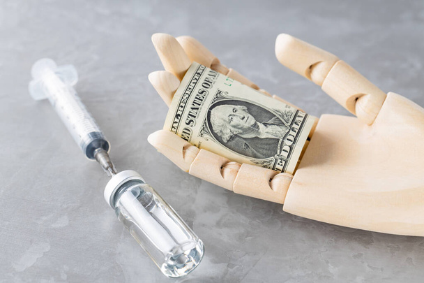 Vaccine, syringe and dollar bill in hand. Wooden hand pays the vaccine. Vaccine purchase concept. Copy space - Foto, imagen
