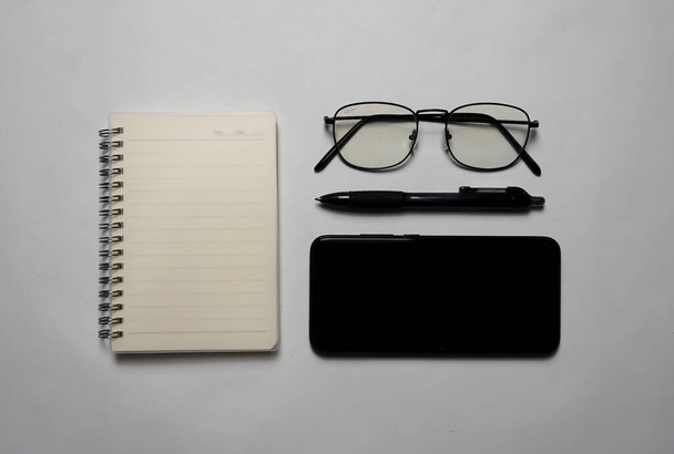 Seen from above there is a notebook with a pen, glasses and a smartphone. - Fotografie, Obrázek