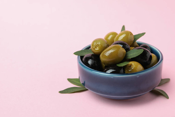 Bol d'olives et de feuilles sur fond rose - Photo, image