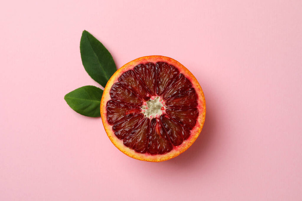 Mitad de naranja roja con hojas sobre fondo rosa - Foto, Imagen