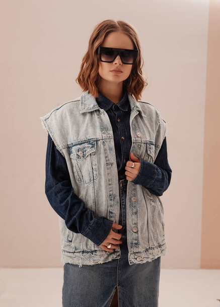 fashion portrait of young confident woman, model, wearing denim jacket and skirt. woman wearing sunglasses. Stylish beautiful woman in denim shirt. total jeans look. studio portrait - Photo, Image