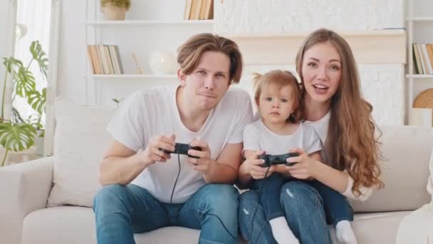 Nadšení běloši rodiče otec a matka s roztomilé dítě dcera batole hráči vítězové hraní videohry na pohovce, vzrušený táta baví s matkou a dítě dívka těší videohry konzole - Záběry, video