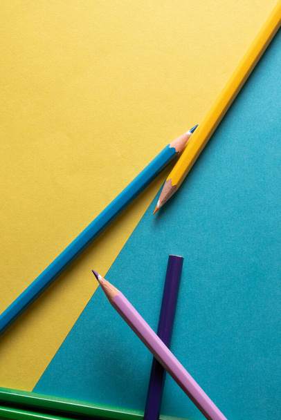 Vue de dessus. Image divisée en deux zones par une diagonale divisant un fond bleu et un fond jaune avec des crayons de couleur. - Photo, image