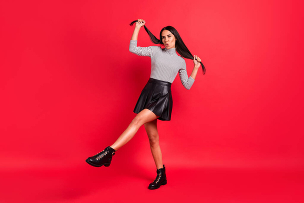 Full length photo of funny cheerful charming lady hold hair tails wear black boots isolated on red color background - Zdjęcie, obraz