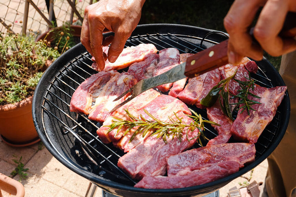 A closeup of a person grilling the steaks with rosemary on the charcoal grill - Foto, immagini