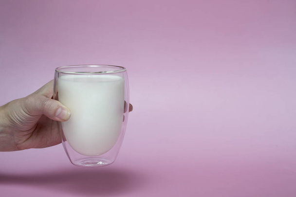 ピンクの背景に乳を入れたグラスを持っている女性の手強化飲料カルシウムミルクの日 - 写真・画像